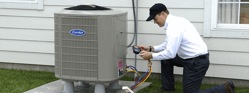 A technician in uniform checks the pressure gauges on an outdoor air conditioning unit next to a house.