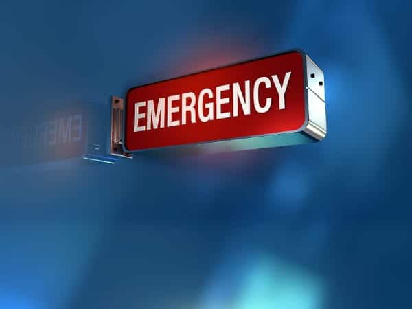 A red, rectangular sign with white letters reads "EMERGENCY," mounted on a wall against a blue, blurred background.