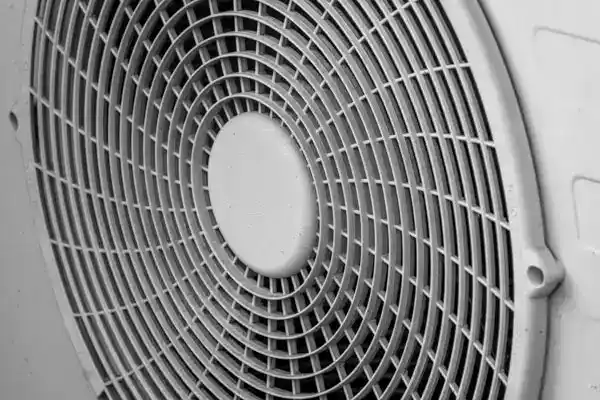 Close-up view of a large, circular fan with a protective metal grid, showing the geometric pattern of the blades and grille.