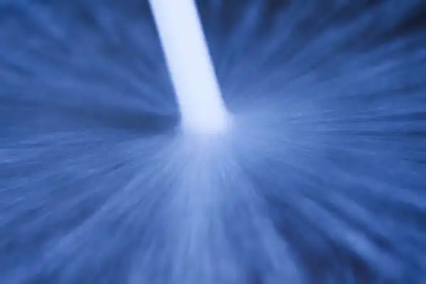 Close-up of a white stream of water or liquid forcefully spraying onto a blue surface, creating a radial splash pattern.
